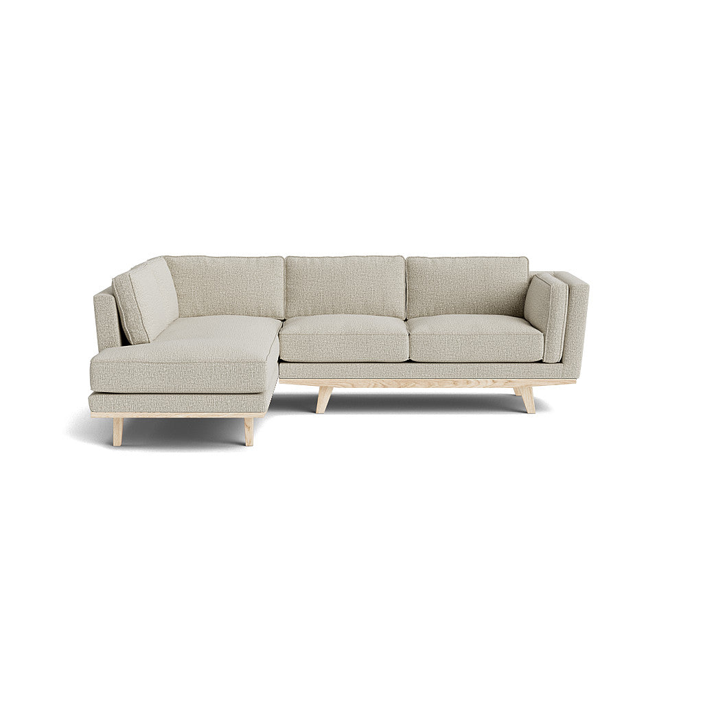 The Kirnik Bumper Sectional in Natural Latex is a beige L-shaped sofa featuring a left-side chaise and light wooden legs, set against a plain white background. It boasts a modern, minimalist design with clean lines and textured upholstery.