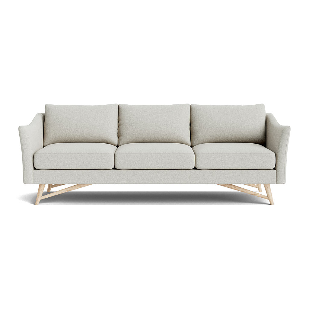 Introducing the Gio Sofa in Natural Latex, a contemporary piece upholstered in light gray fabric with three cushions and angled wooden legs. It boasts gently curved armrests and a sleek design, perfect for modern interiors.