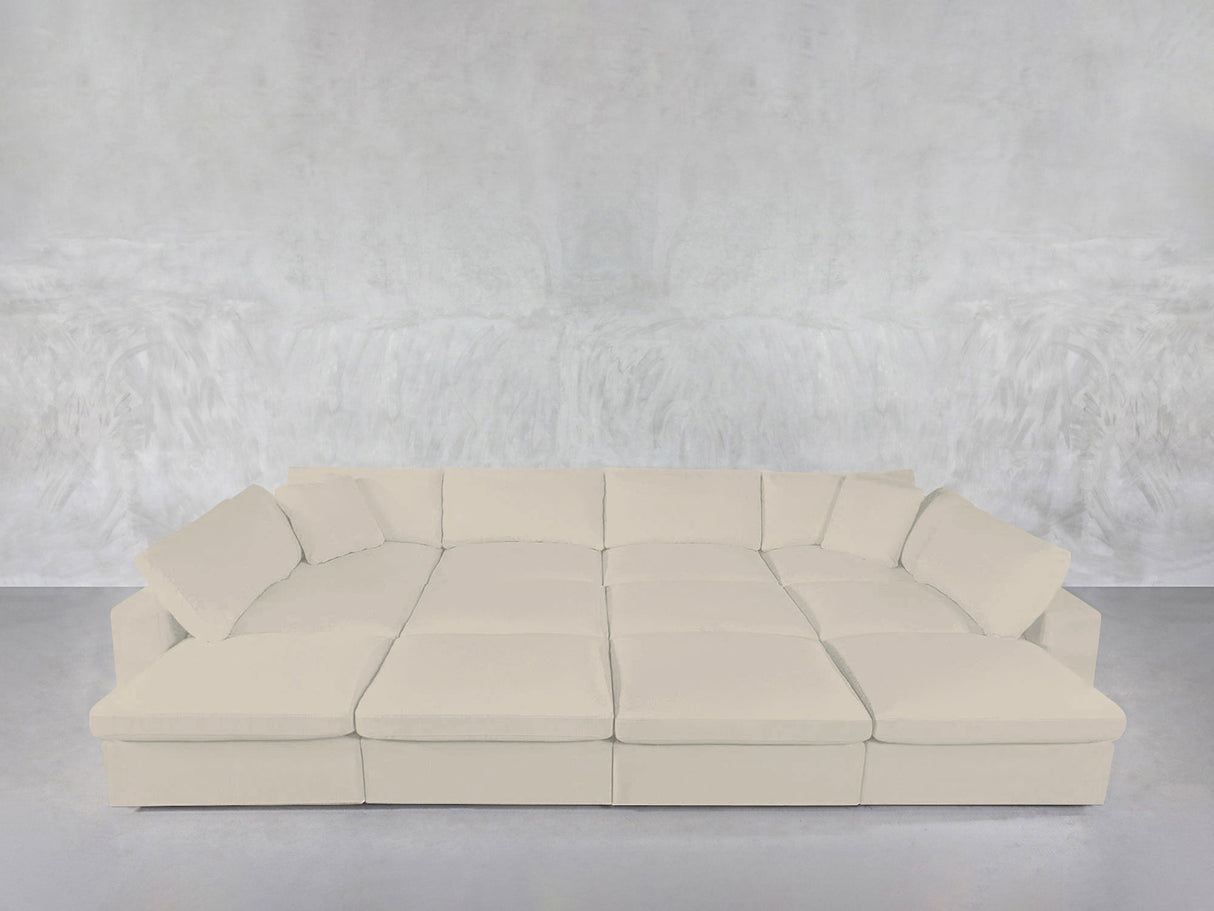 The 12-Seat Deep Modular Daybed, in a modern cream tone with multiple cushions, is arranged against a textured light gray wall and floor for a minimalistic, contemporary vibe.