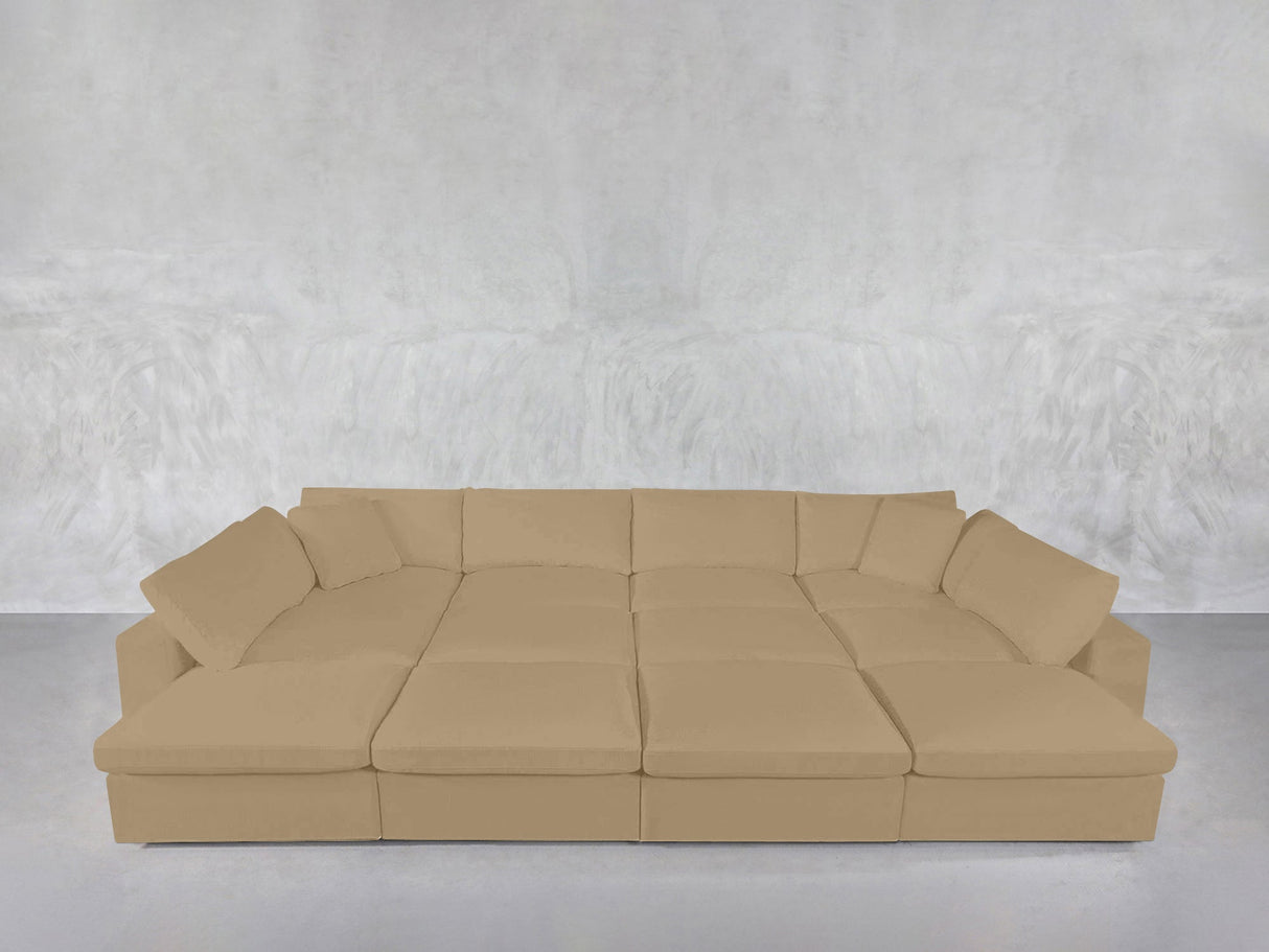 A 12-Seat Deep Modular Daybed in beige with multiple cushions is arranged against a textured light gray wall and rests on a smooth, light gray floor.