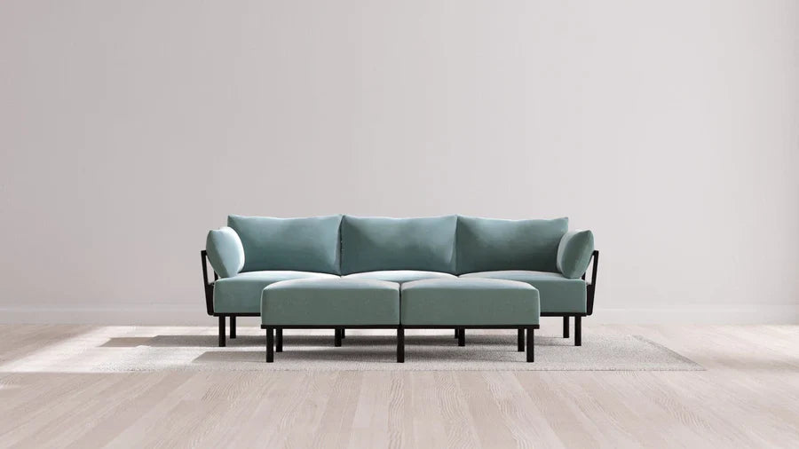 A modern living room with an Indoor Jack 3-Seater Sofa and Bench Ottoman in Balsa resting on a textured rug. The space features a minimalist design with a light wood floor and neutral wall backdrop, creating a clean and serene atmosphere.