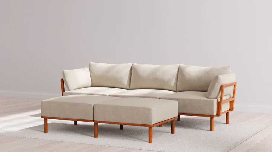 The Indoor Jack 3-Seater Sofa + Bench Ottoman in Balsa, featuring a modern design with a wooden frame and cushions, is styled with two matching ottomans on a light-colored rug in a minimalist setting with wooden flooring and neutral walls.