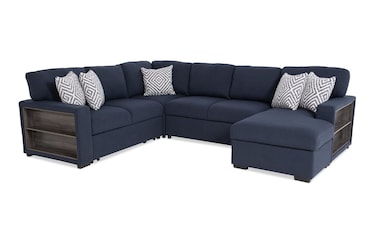 A beige L-shaped sectional sofa with built-in USB and USB-C ports on the sides. It includes multiple gray and white geometric-patterned throw pillows.