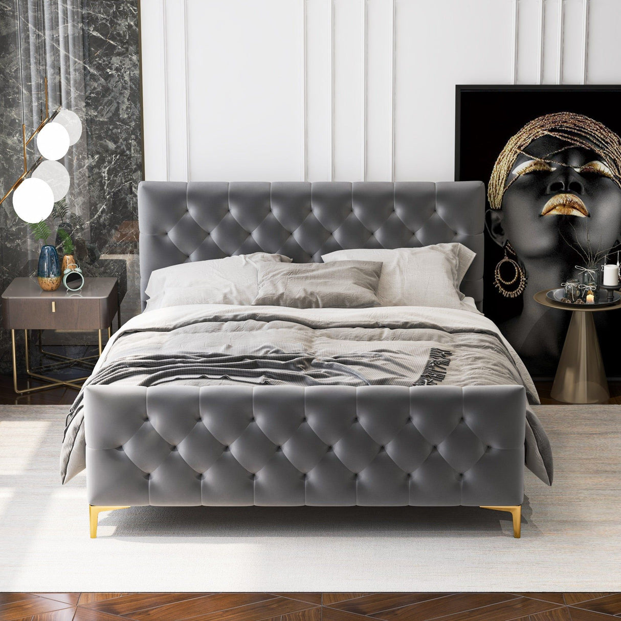 A luxurious bedroom featuring the Bailey - Elegant Design Bed in gray tufted fabric sits on a patterned rug. The room includes elegant bedding in neutral tones, a modern lamp atop a side table, and a large artistic portrait with golden accessories against a dark background resting on the floor.