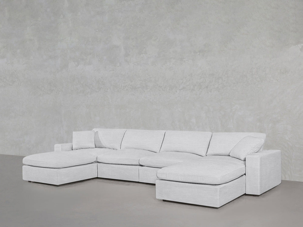 A 6-Seat Modular Double Chaise Sectional in light gray with plush cushions sits on a smooth gray floor against a textured light gray wall.