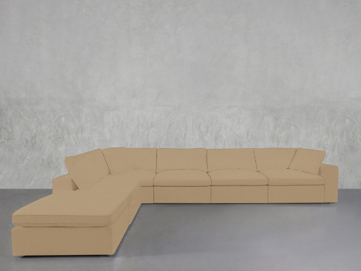 A 6-Seat Modular Corner Lounger Sectional in beige, featuring multiple cushions, is arranged against a plain light-gray textured wall on a smooth gray floor.