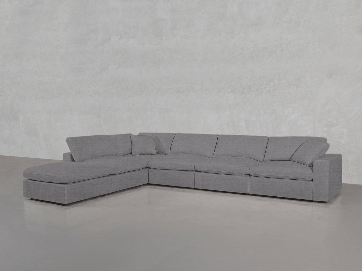 A spacious 6-Seat Modular Corner Lounger Sectional in light gray with wide cushions and a chaise lounge is placed on a smooth concrete floor against a textured light gray wall.