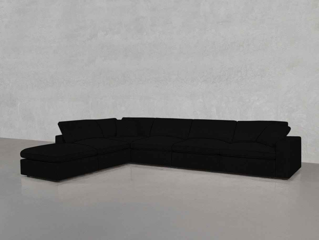 A spacious, modern 6-Seat Modular Corner Lounger Sectional in black with a left-side chaise is positioned in an empty room featuring light grey walls and a smooth grey floor.
