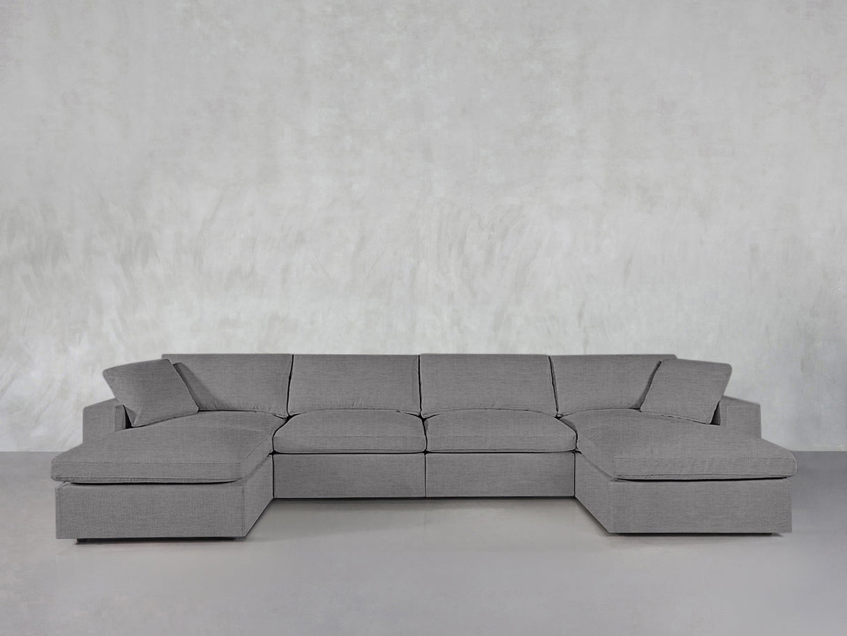 The 6-Seat Modular Double Chaise Sectional in modern gray, featuring wide armrests and cushions, sits against a light gray textured wall in a minimalist space.