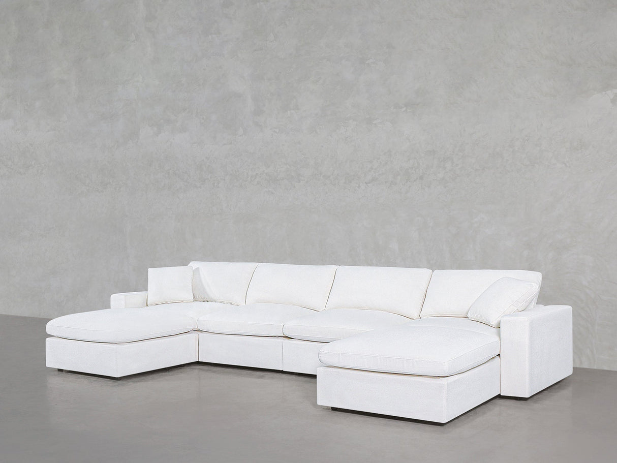 The 6-Seat Modular Double Chaise Sectional, featuring clean lines and plush cushions, is arranged against a light gray textured wall on a smooth floor.