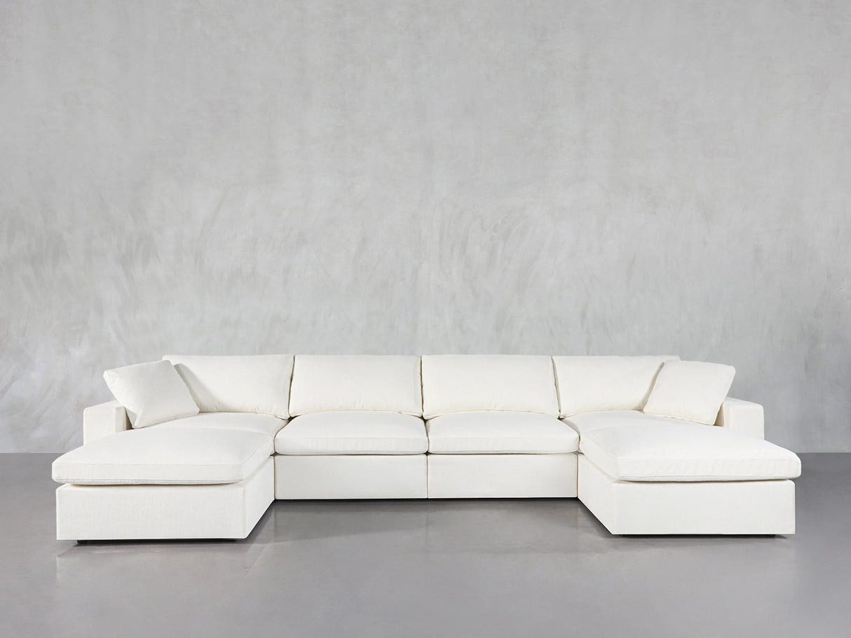 The 6-Seat Modular Double Chaise Sectional, featuring wide seats, plush cushions, and chaise lounges on both ends, is showcased against a plain light gray wall and a smooth gray floor.