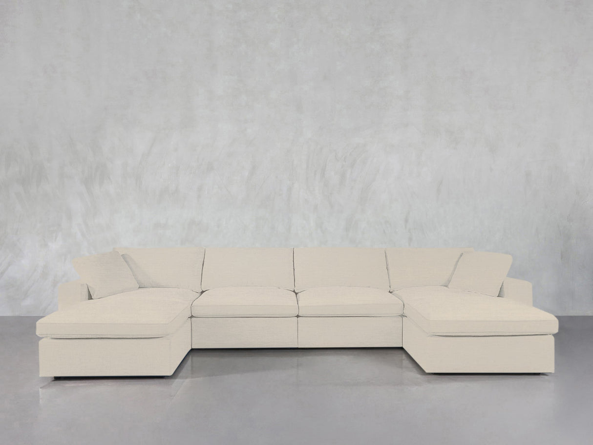 A 6-Seat Modular Double Chaise Sectional in light beige with clean lines and plush cushions sits against a textured light gray wall atop a smooth gray floor.
