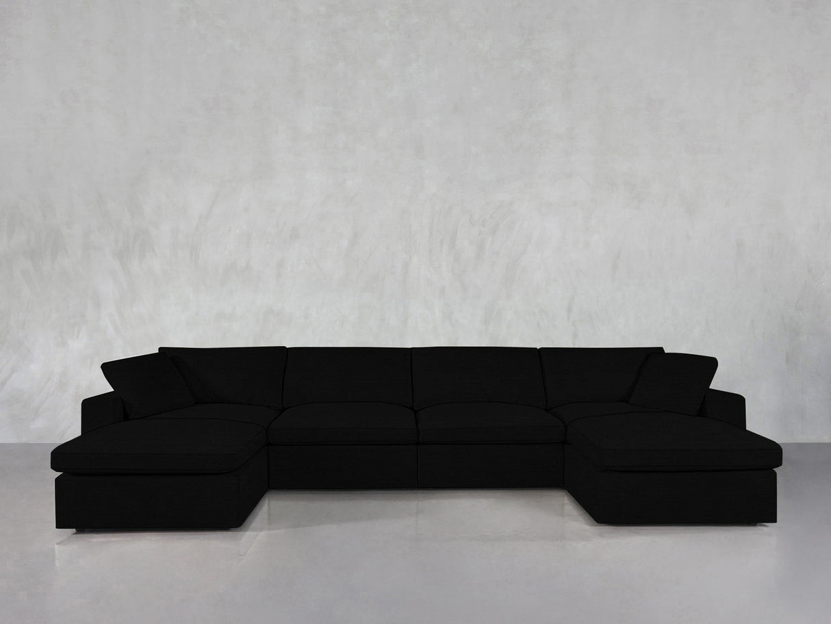 The 6-Seat Modular Double Chaise Sectional, featuring wide seats and low backrests in modern black, is arranged against a light gray textured wall and a smooth, reflective floor.