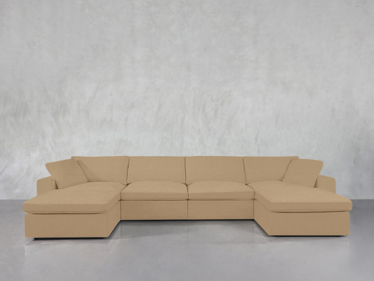 A 6-Seat Modular Double Chaise Sectional in beige sits against a light gray textured wall, with its two chaise lounges on either end. The floor beneath is smooth and reflective.