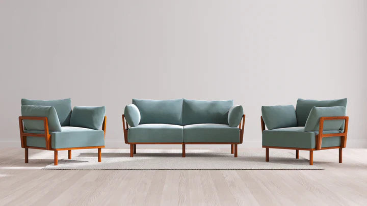 A contemporary setup consisting of the Indoor Jack 2-Seater Sofa and Armchair Set in Balsa, adorned with teal cushions and wooden frames. The set is placed on a light-colored area rug atop a wooden floor, against a plain light gray wall.