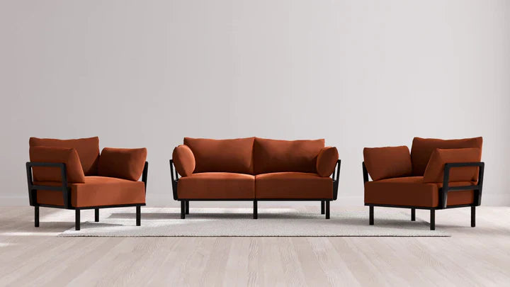 A contemporary living room ensemble showcases the Indoor Jack 2-Seater Sofa and Armchair Set in a warm Balsa shade. They are paired with black-framed armchairs, all positioned on a light gray rug atop a wooden floor against a plain gray wall.