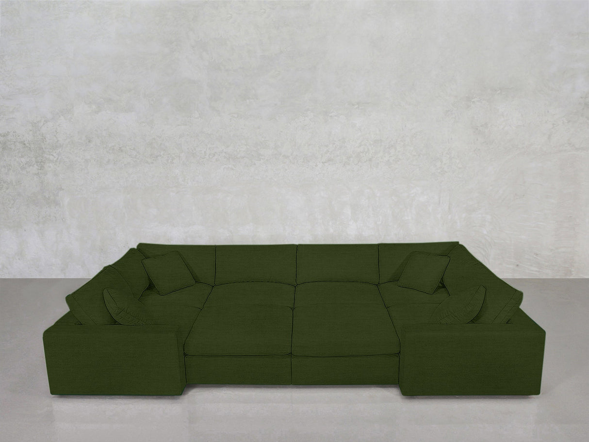 The 8-Seat Modular Closed Pit, in deep green with wide seats and matching pillows, sits before a smooth, light gray textured wall on a pale floor.