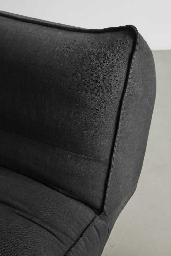 Close-up of the Greta XL Sleeper Sofa in dark gray fabric set against a light gray background. The focus is on the corner of the sofa, highlighting its stitched edges and cushioned backrest.