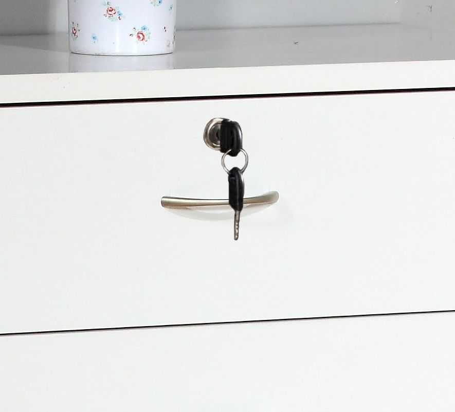 A 5 Drawer Chest in white with metal handles features a locking top drawer with a key inserted. A white container with a floral design is partially visible on the shelf above.