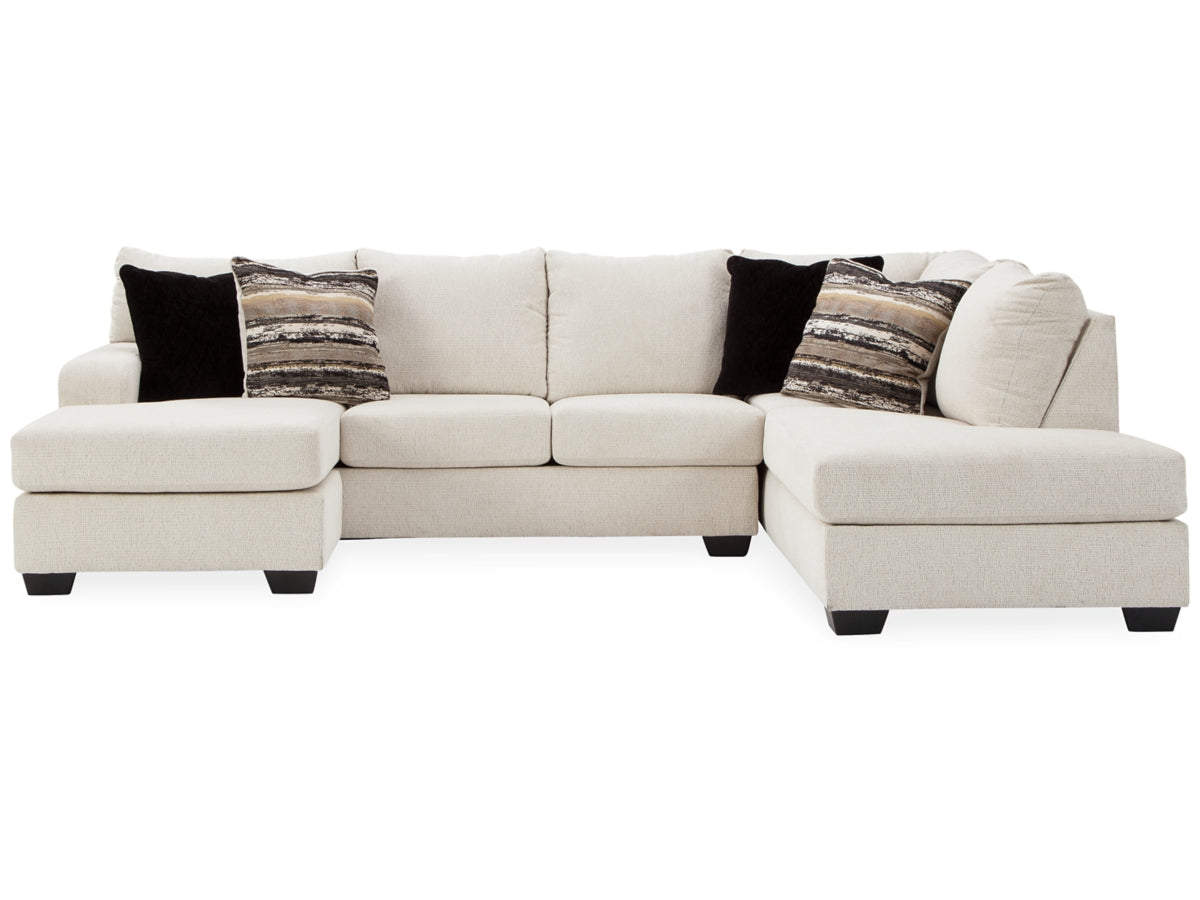 The Cambri 2-Piece Sectional with Chaise is a large beige sofa featuring a left-side chaise lounge, four seats, and black square wooden legs. It comes adorned with two patterned and two solid black throw pillows. The plush cushions add to its comfortable appearance.