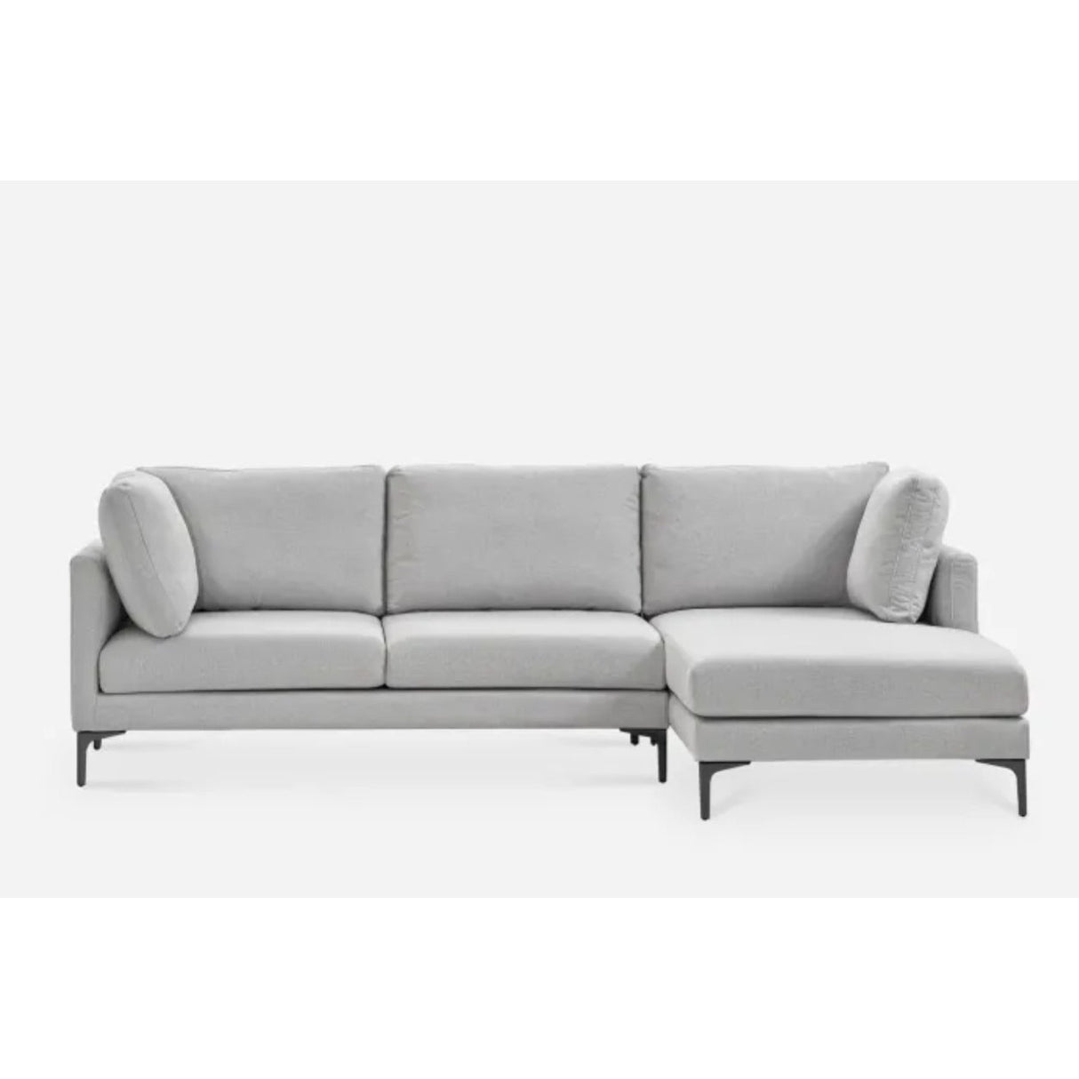A modern L-shaped light gray sectional sofa with three seat cushions, an attached chaise on the right side, and two cylindrical throw pillows. The sofa has a minimalist design with slender black legs, set against a plain white background.
