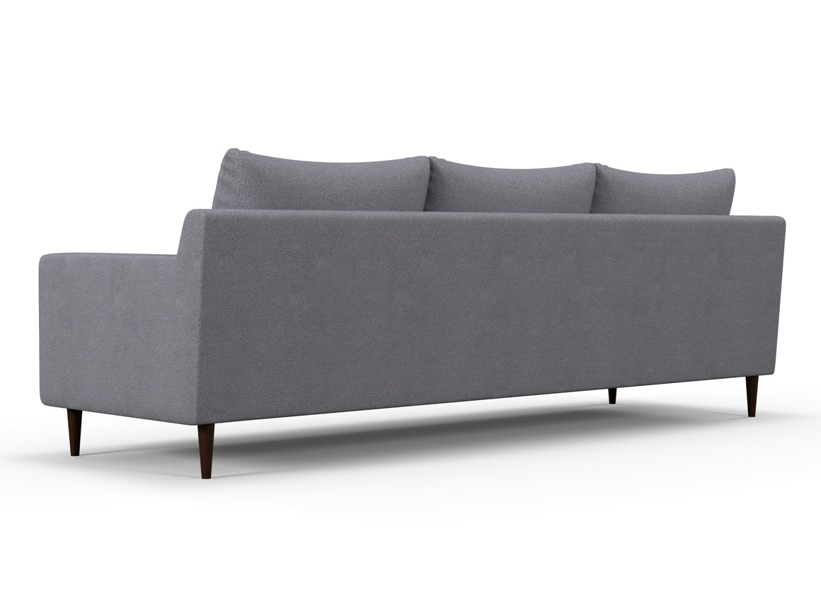 The Alex Sofa is a contemporary piece with a minimalist design, featuring three cushions and a low backrest. It stands on dark, tapered wooden legs, presenting a sleek modern look when viewed from the back at an angle.