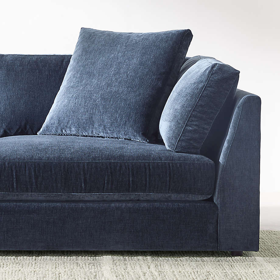 The Monterey Modular 3 Piece L Shaped Sectional Sofa in dark blue fabric is positioned against a white wall. It rests on a light gray textured rug, highlighting a cozy and minimalist interior design.