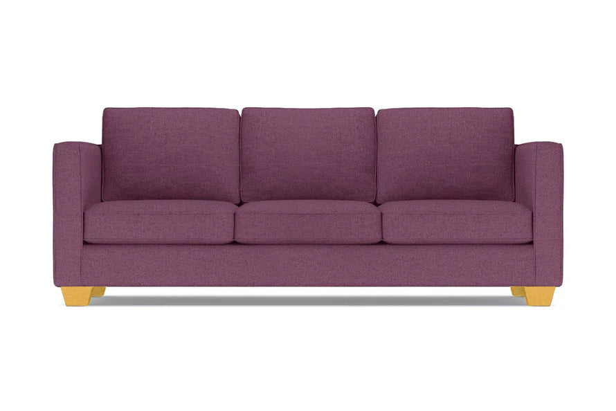 The Catalina Sofa, with its modern design in a purple hue, comes complete with three cushions. It features straight arms and light wooden legs, all showcased against a white background.