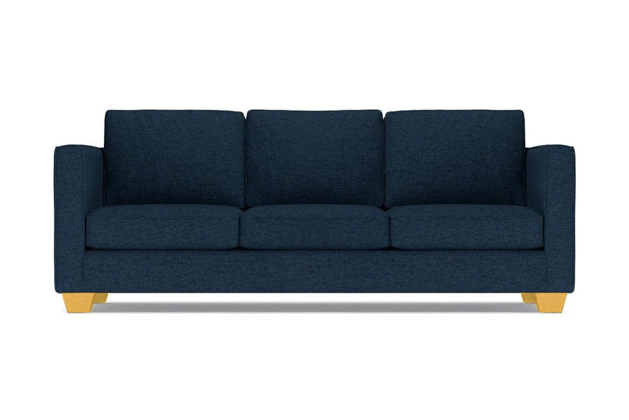 The Catalina Sofa is a dark blue three-seater featuring square cushions and light wooden legs, set against a white background.