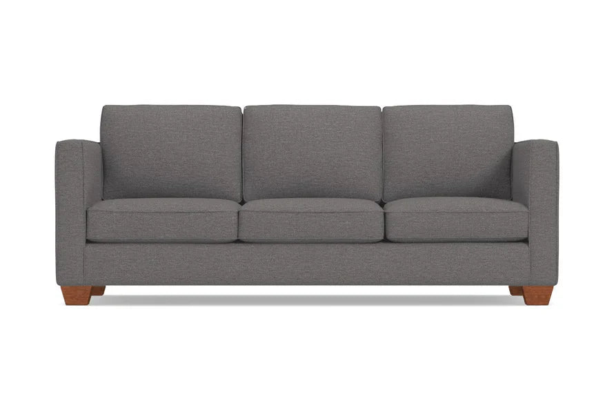 The Catalina Sofa is a gray, three-seater piece with a minimalist design and wooden legs. It features straight arms and three back cushions, set against a plain white background.