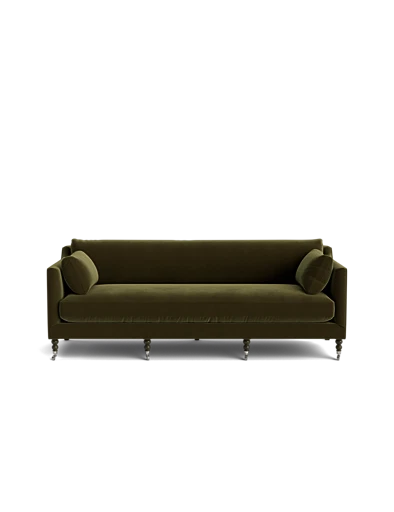 The Fabienne Sofa, in a luxurious green velvet, comes with two matching round pillows. It features a classic design and wooden legs, all showcased against a plain black background.