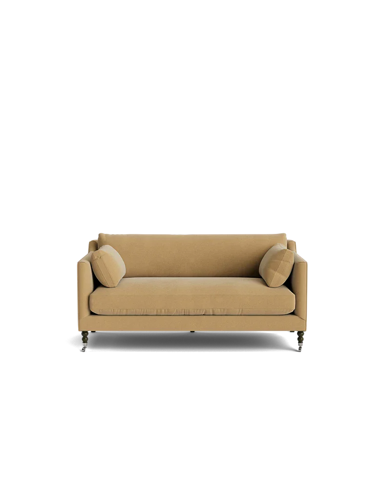 The Fabienne Sofa, featuring a modern design with thin armrests and small, rounded legs, is displayed against a solid black background alongside two matching round beige cushions.