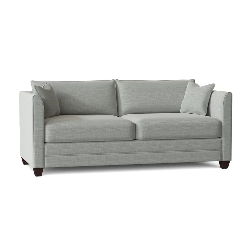 The Kodie 76.5" Upholstered Sleeper Sofa features a light gray fabric, complemented by two matching cushions. Its slim armrests and dark wooden legs add to the modern and minimalist aesthetic.