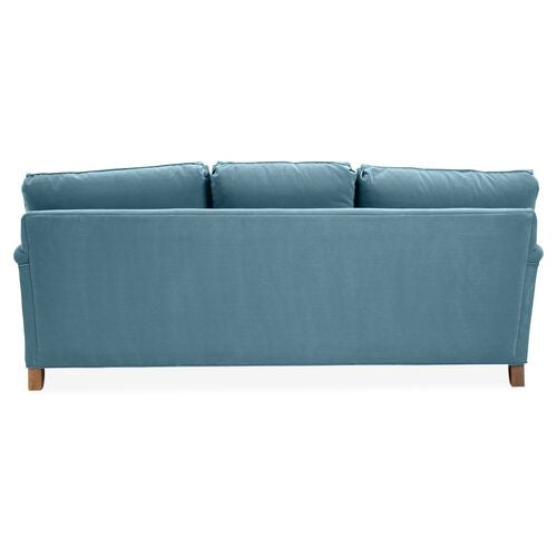 A Brooke 6-Seat Sofa featuring a blue design with three cushioned backrests, seen from behind. It boasts a simple design complemented by wooden legs.