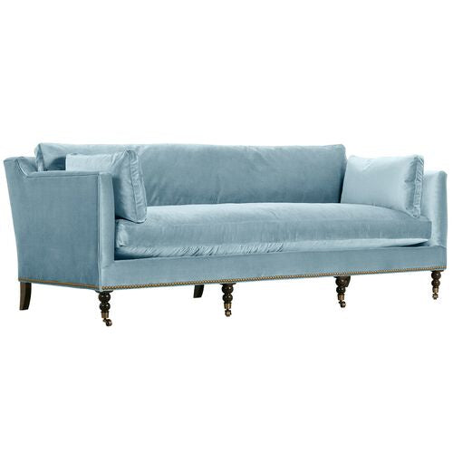 The Margot Velvet Sofa is a light blue piece with plush cushions and dark wooden legs, showcasing a modern design with a high back and armrests.