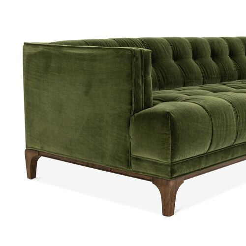 Displayed is the Caledonia Sofa in Sapphire Olive Velvet, featuring a modern design with tufted upholstery. It boasts a low back and seat paired with wooden legs, visible from a side angle.