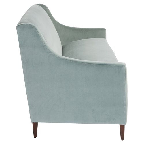 A side view of the Dawes Sofa in Sage Velvet showcases its smooth curves and wooden legs, set against a plain white background.