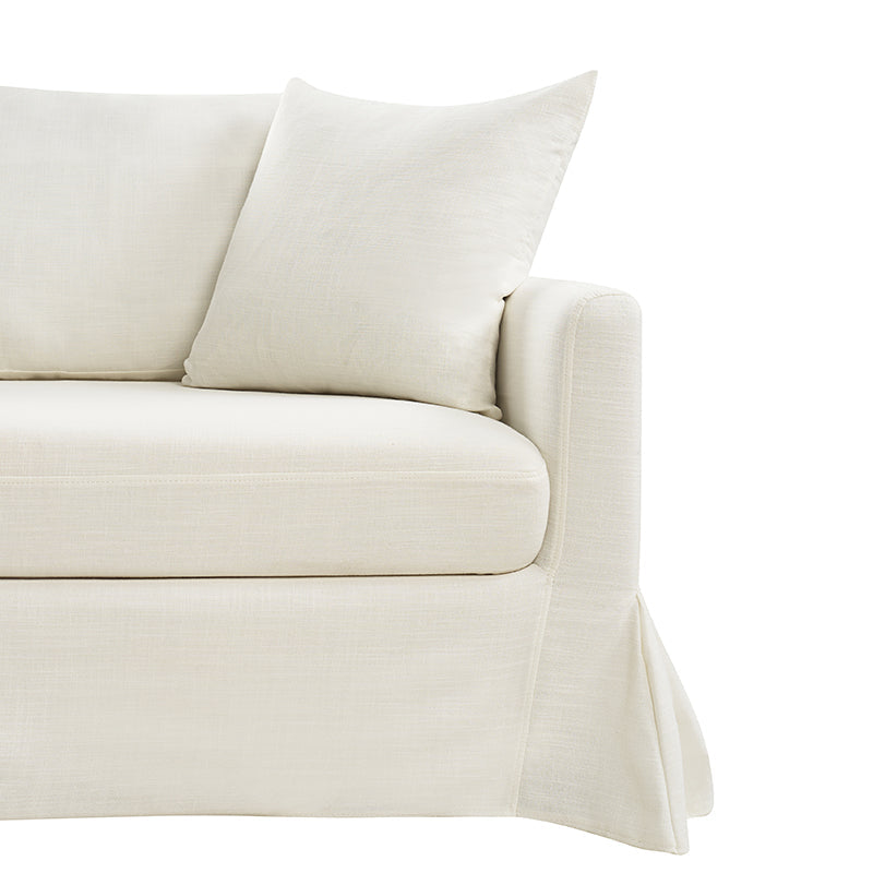 A close-up view of the Torsten Modern Comfortable Sofa in a cream color, featuring a skirted base and a matching cushion. The soft and plush fabric gives it a cozy and inviting appearance. The armrest is slightly rounded, set against a white background.