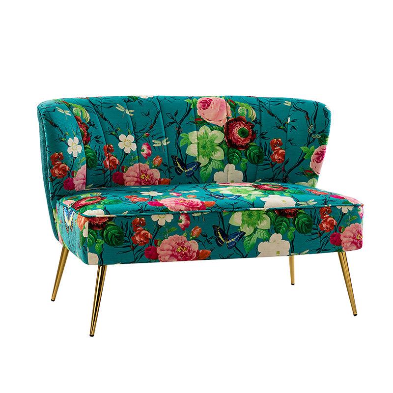 The Coraline Loveseat features a vibrant teal upholstery with a lively floral pattern, adorned with bright flowers and butterflies. It boasts a curved backrest and elegant gold-colored legs.