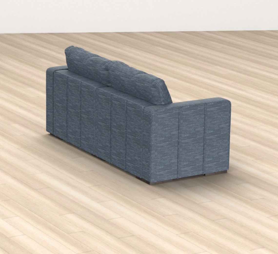 A vintage blue chenille Sactional, featuring two seats and four sides, is situated on a light wood floor. The image is taken from behind, highlighting the sofa's clean lines and textured fabric in a minimalistic setting.