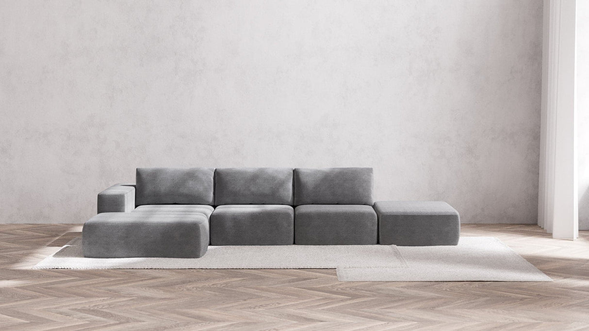 A minimalist living room showcases the Modular 3-Seater Open-End Chaise Sectional in Boucle Aspen, positioned on a light area rug. The space is enhanced by a hardwood herringbone floor and plain white walls, with natural light streaming in from the right side.
