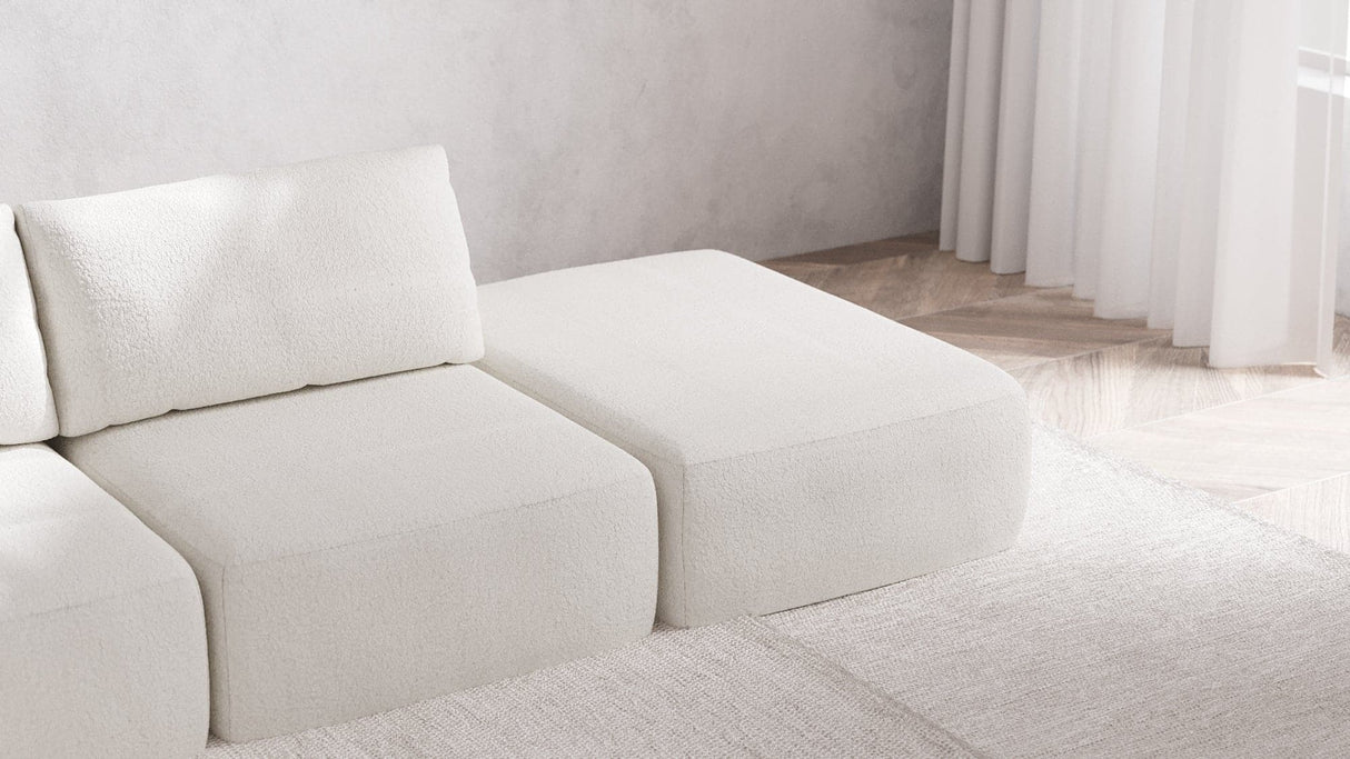 A minimalist living room showcases the Modular 3-Seater Open-End Chaise Sectional in Boucle Aspen, elegantly placed on a white rug. The space is enhanced by light wood flooring and sheer white curtains, contributing to a bright and serene atmosphere.