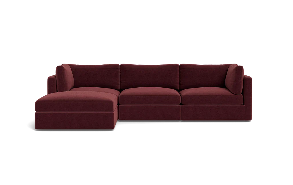 The Tatum Modular 3 Seat Chaise Sectional, upholstered in maroon, sits against a solid black background. It boasts plush cushions and a chaise lounge on the left side, providing a modern and comfortable seating option.