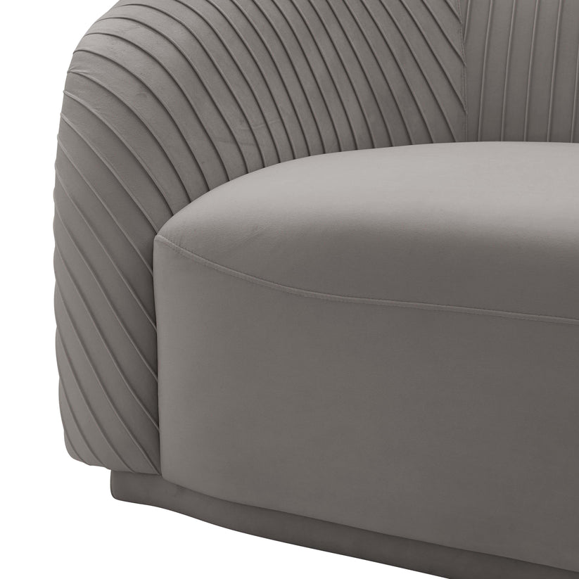 Close-up of the Yara Pleated Velvet Sofa by Inspire Me! Home Decor, showcasing its modern gray hue with textured pleating on the armrests and a smooth seat cushion. The design features a minimalist, curved shape that emphasizes contemporary style.