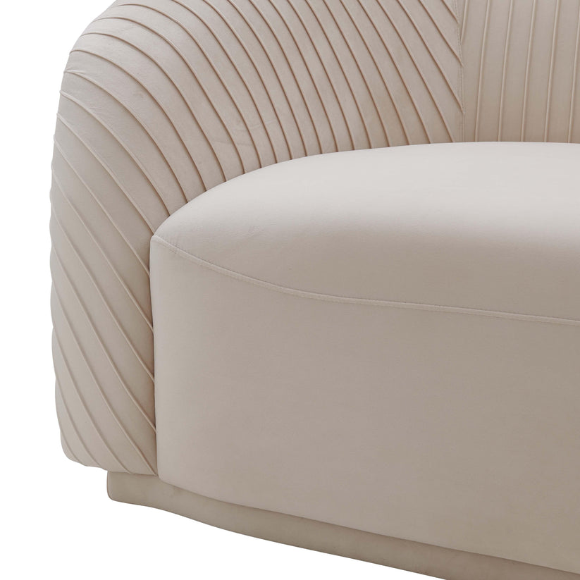 A detailed view of the Yara Pleated Velvet Sofa by Inspire Me! Home Decor, showcasing its cream color and rounded, cushioned backrest. The linear, ribbed texture on the sides enhances the elegance of its contemporary design.