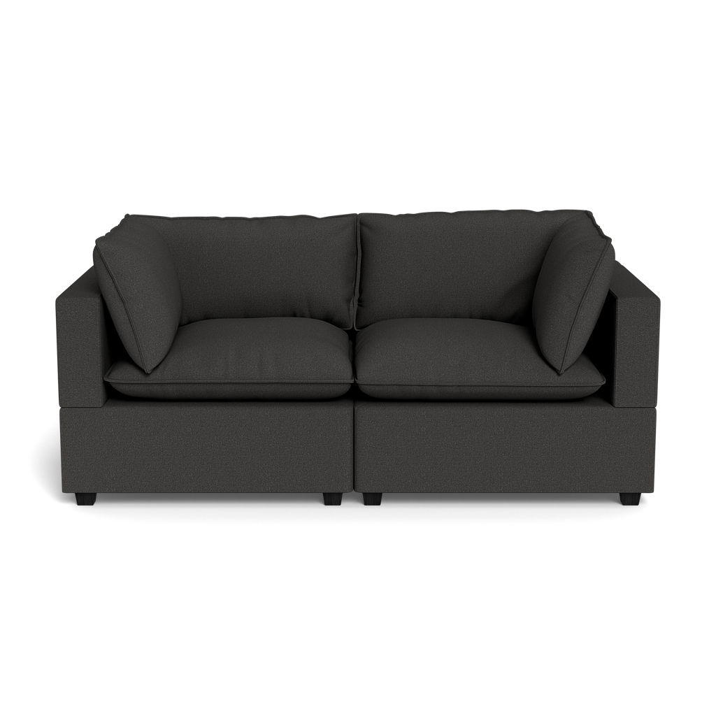 The Kova Pillow Cushion Sofa 86" is a modern dark gray fabric sofa with wide armrests, two large seat cushions, and two matching back cushions, shown from the front against a black background.