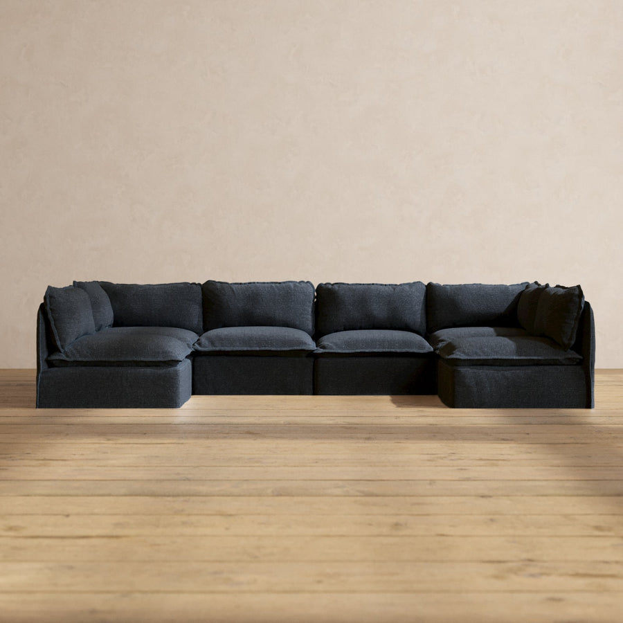 The Modular Performance 6-Seater Open-Ends U-Sectional in Plush Weave Ash is positioned against a beige wall and rests on a light wood floor. Its minimalist design fosters a modern and cozy atmosphere.