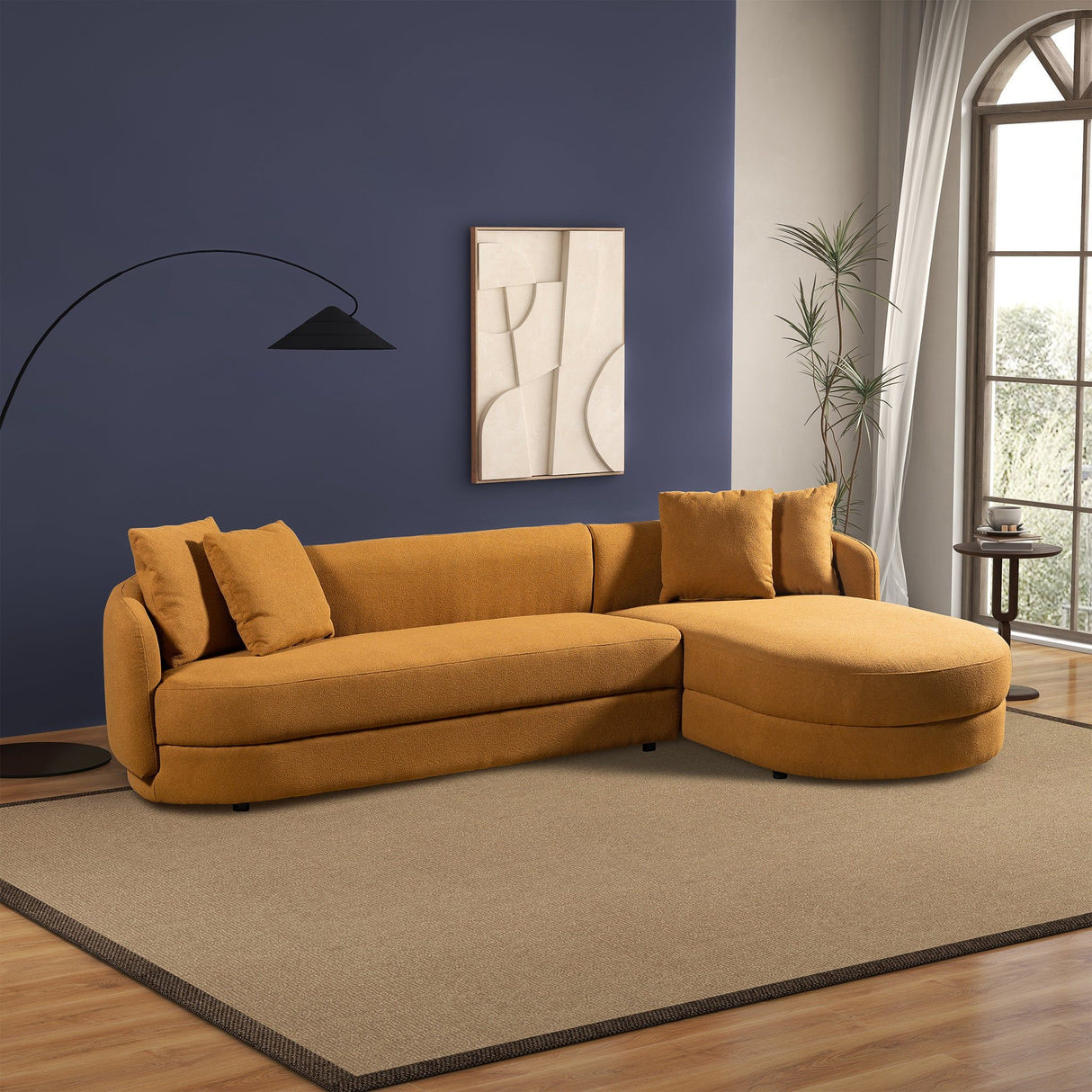 A modern living room showcases the Chandler - Comfortable Sectional Sofa in mustard-yellow on a beige rug, complemented by a black-shaded floor lamp, an abstract artwork on a dark blue wall, and light curtains framing a large window with greenery views.