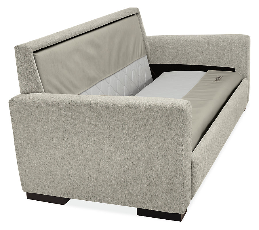 The Berin Day & Night Sleeper Sofa is a contemporary gray piece featuring sleek, angular arms and prominently displayed cushioning. The sofa includes a backrest adorned with patterned fabric and stands on dark wooden legs.