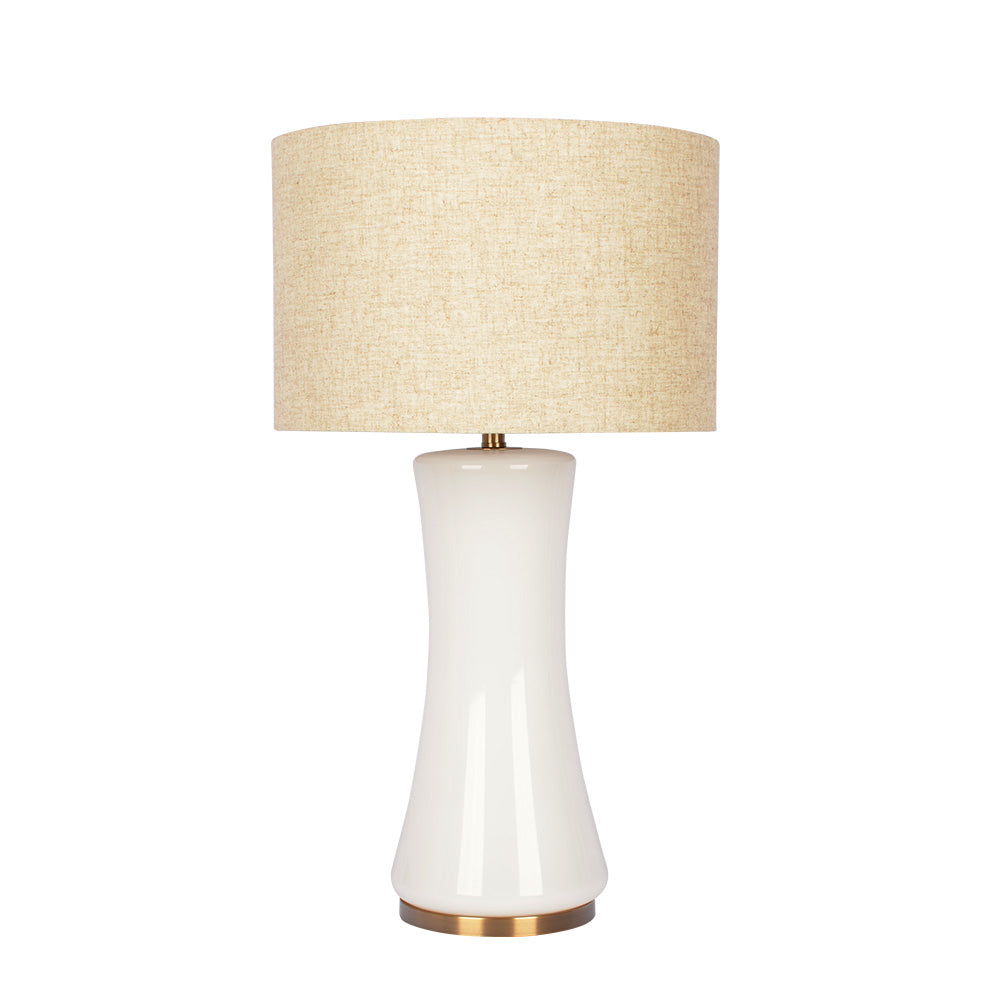 The Cascade lamp features a sleek white ceramic base with an hourglass shape, a beige fabric drum shade, and a brass-colored platform.